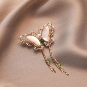 Elegant butterfly brooch with shell wings, pearls, and tassels on silk fabric backdrop