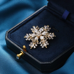Broche flocon de neige dorée rotative avec cristaux de zircone sur velours bleu