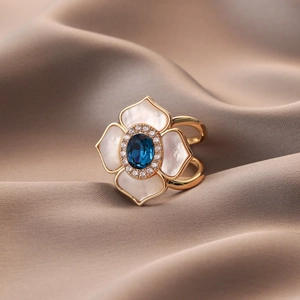 Elegant gold flower ring with blue gemstone and white shell petals on champagne satin