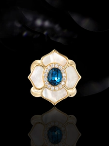 Detail of flower shaped ring with gold edges, white petals and central blue gemstone