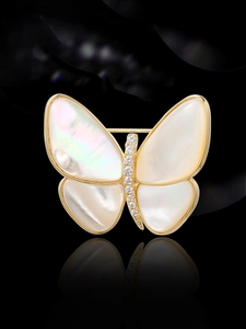 Macro shot of butterfly brooch with white shell wings and zircons on gold plating