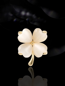 Détail de la broche fleur à quatre feuilles dorée avec pierres œil-de-chat sur fond noir poli