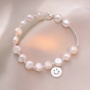 Macro detail of S925 sterling silver smile charm and irregular freshwater pearl bracelet
