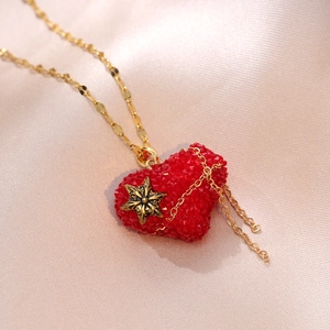 Détail du pendentif cœur rouge avec motif étoile sur chaîne dorée et soie champagne