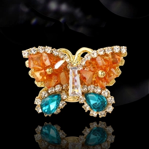 Elegant gold butterfly brooch with orange and blue crystals on a reflective black background