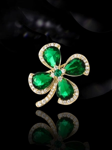 Detailed macro of gold four-leaf clover brooch with emerald gemstones and white zircons