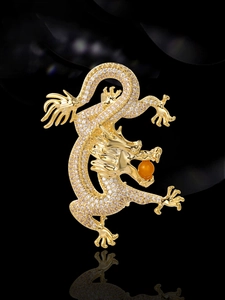 Macro detail of a golden dragon brooch with micro-pave zircons and an orange gemstone bead