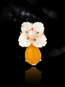 Detailed close-up of a shell flower brooch featuring a pearl center and a pear-cut orange gem