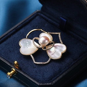 Elegante gouden bloemspeld met parelmoer blaadjes en parel op blauw fluweel