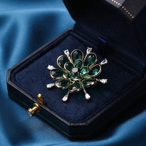 Elegant gold-tone flower brooch with emerald green crystals on dark velvet jewelry box