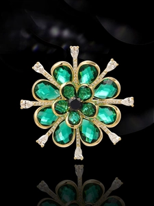 Macro shot of emerald green flower brooch with gold base and zircon stones on black glass