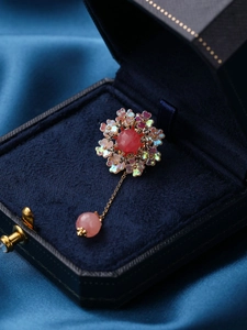 Detailed view of a vintage flower brooch with pink stone and tassel in a blue velvet box