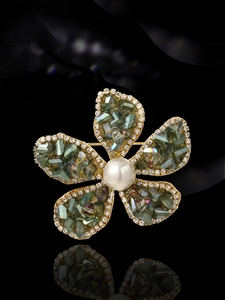Detailaufnahme einer goldenen Blumenbrosche mit grünen Kristallen und einer Perle