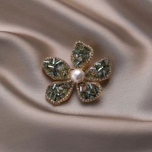 Eleganter goldener Blumenbroschen mit grünen Kristallen und Perle auf Seidenhintergrund