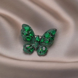 Vintage emerald green crystal butterfly brooch with gunmetal finish on satin background