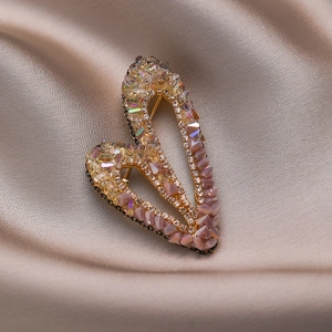 Broche de corazón asimétrico con circonitas de colores y borlas sobre seda champán