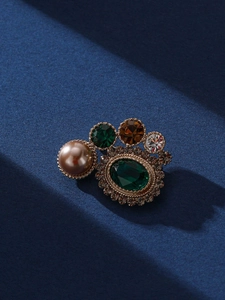Détail d'une broche vintage avec pierre émeraude, perle et texture tissée dorée