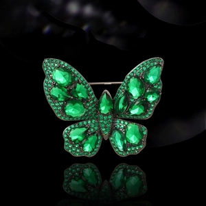 Vintage butterfly brooch with emerald green crystals and black gold frame on black reflection