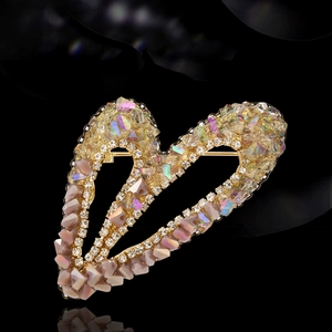 Elegante broche de corazón con circonitas de colores y borlas en fondo negro liso