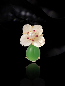 Macro shot of shell flower brooch with white pearl and green teardrop gemstone detail