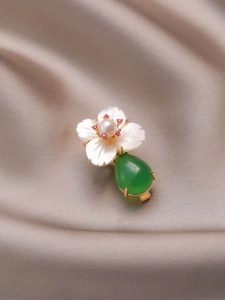Detail of vintage flower brooch with white shell petals, pearl, and green drop pendant