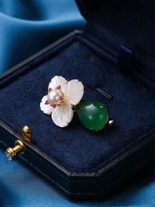 Macro detail of white shell flower brooch with pearl center and green teardrop gemstone