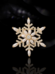 Detailed macro view of golden snowflake brooch with pearls and zircon on black background
