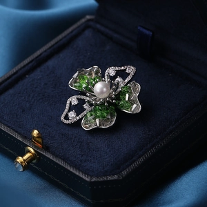 Elegant floral brooch with white pearl and green crystals on deep blue velvet box