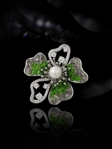 Macro shot of elegant silver flower brooch with green crystals and a glossy white pearl