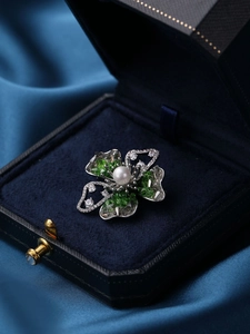 Macro shot of silver flower brooch with green crystals and pearl in a jewelry box