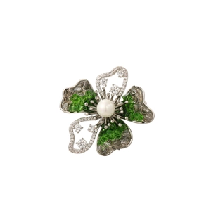Detailed view of flower brooch with green crystals, white pearl, and silver finish