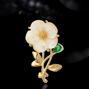 Elegant floral brooch with shell petals, golden accents and a green gemstone drop charm