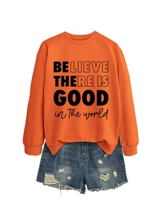 Dettaglio della felpa arancione con scritta BELIEVE e pantaloncini in denim usurati