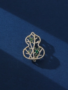 Macro shot of gold hollow gourd brooch with bamboo motif and green gemstones
