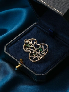 Detail of a hollow gourd brooch with gold metal frame and white and olive green gems