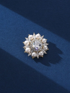 Gros plan d'une broche florale avec base dorée, perles blanches et cristaux brillants