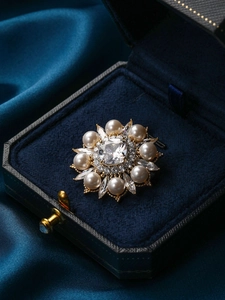 Détail macro d'une broche fleurie avec pierre carrée, perles et écrin de velours bleu