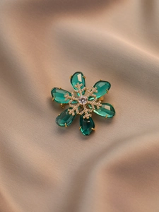 Detail of emerald snowflake brooch with gold metal frame and sparkling micro-inlaid stones