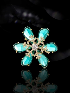 Macro shot of snowflake brooch with gold petals, clear center stone and green gems