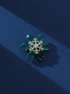 Detail of a snowflake brooch featuring green drop crystals and golden pavé diamonds