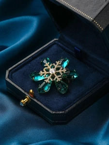 Close-up of golden snowflake brooch with green pear-cut gems and sparkling zircons