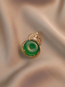 Vista macro del broche vintage con piedra verde, perlas y detalles de filigrana dorada
