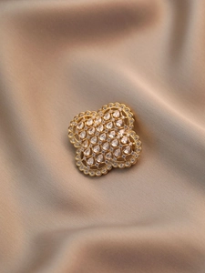 Vue macro de la broche trèfle dorée ajourée avec zircons sur un tissu en soie fluide