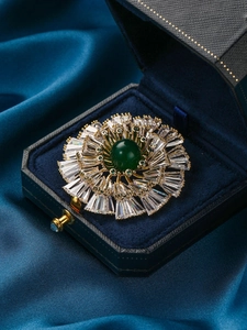 Macro view of floral brooch with green center stone and crystals in a jewelry box
