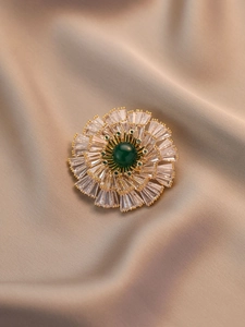 Detail of vintage flower brooch with green gemstone and clear zircon petals on silk