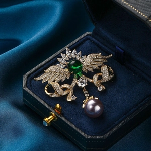 Elegante Engelsflügel-Brosche mit grünem Edelstein und grauer Perle in Schmuckschatulle