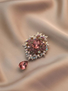 Detailed view of flower brooch with pink crystals and pear-shaped drop on satin