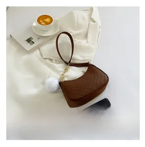 Sac bandoulière marron matelassé en suédine avec pompon blanc sur fond de veste blanche