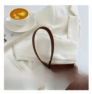 Détail de la bandoulière en daim marron avec chaîne dorée sur une veste blanche chic