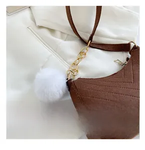 Détail du sac bandoulière en daim marron foncé avec chaîne dorée et pompon blanc